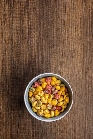 Colorful breakfast cereals in a bowl on a wooden table. Top view.