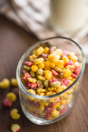 Colorful breakfast cereals in the shape of various fruits in a jar on a wooden table.