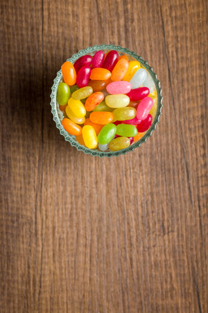 Multicolored jelly beans with various flavors in a glass bowl on a wooden table. Top view.の写真素材