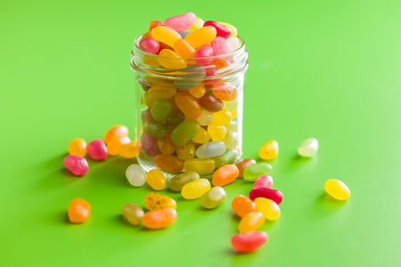 Multicolored jelly beans with various flavors in a jar on a green background.の写真素材
