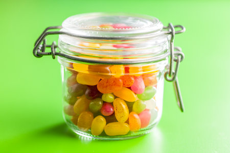 Multicolored jelly beans with various flavors in a jar on a green background.の写真素材