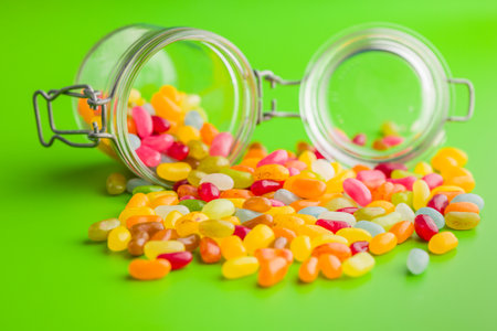 Multicolored jelly beans with various flavors in a jar on a green background.の写真素材