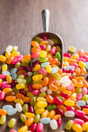 Multicolored jelly beans with various flavors in a scoop on a wooden table.の写真素材