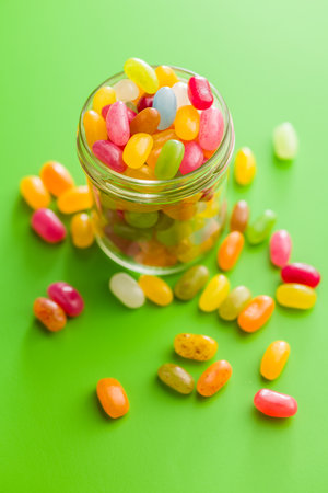 Multicolored jelly beans with various flavors in a jar on a green background.の写真素材
