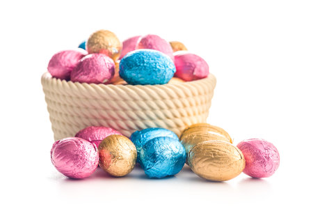 Chocolate easter eggs wrapped in multi colored foil in a bowl isolated on a white background.の写真素材