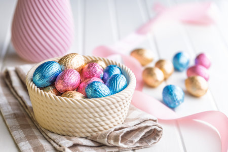 Chocolate easter eggs wrapped in multi colored foil in a bowl on a white table.の写真素材