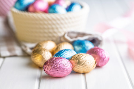 Chocolate easter eggs wrapped in multi colored foil on a white table.の写真素材
