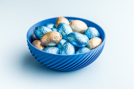 Chocolate easter eggs wrapped in multi colored foil on a blue background.の写真素材