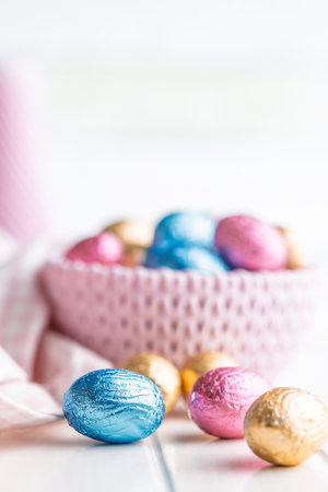 Chocolate easter eggs wrapped in multi colored foil on a white table.の写真素材