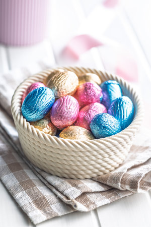Chocolate easter eggs wrapped in multi colored foil in a bowl on a white table.の写真素材