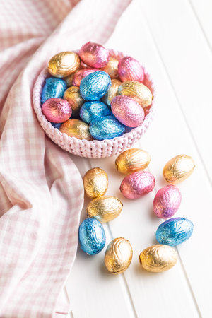 Chocolate easter eggs wrapped in multi colored foil in a bowl on a white table.の写真素材