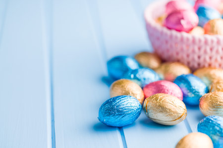 Chocolate easter eggs wrapped in multi colored foil on a blue table.の写真素材