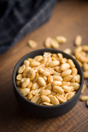 Roasted salted peanuts in a bowl on a wooden table.