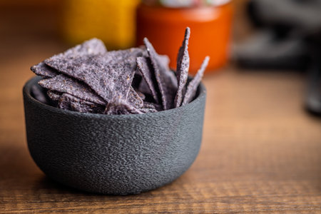 Dark nachos chips in a bowl on a wooden table.の写真素材