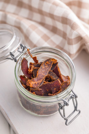 Beef jerky. Dried spiced meat in a jar on a white table.の写真素材
