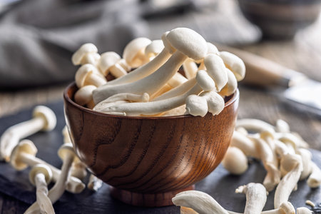 Raw white shimeji mushrooms in a bowl on a cutting board.の写真素材