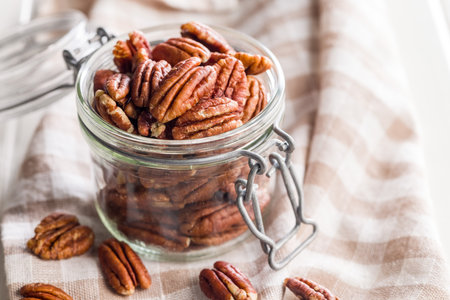 Peeled pecan nuts in a jar on a white table.
