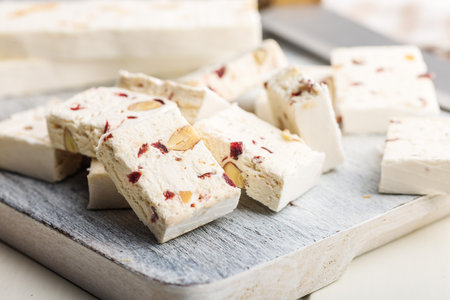 White nougat bars with almonds and dried fruit on a cutting board on a white table.の写真素材