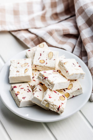 White nougat bars with almonds and dried fruit on a plate on a white table.の写真素材
