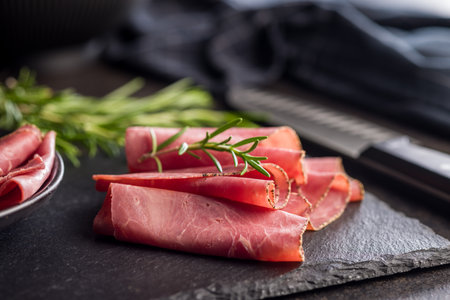 Sliced beef pastrami on a cutting board on a black table.の写真素材