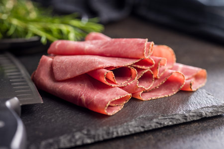 Sliced beef pastrami on a cutting board on a black table.の写真素材
