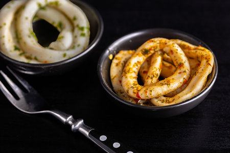 Marinated squid rings in a bowl on a black table.