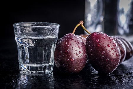 Plums and distilled alcohol on a black table. Plum brandy shot.の写真素材