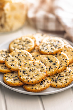 Crispy round salted crackers with sesame seeds on a plate on a white table.の写真素材