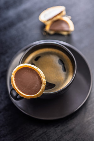 Sweet chocolate tartelettes and coffee cup on a black table.の写真素材