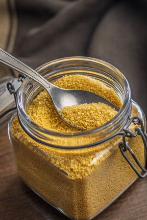 Uncooked couscous in a jar on a wooden table.