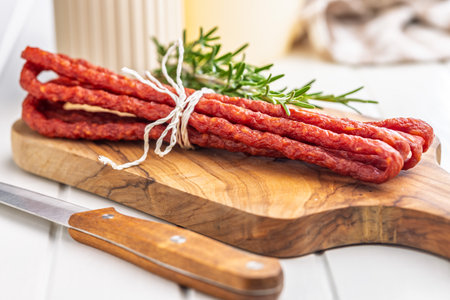 Smoked cabanos. Mini dried thin sausages on a cutting board.