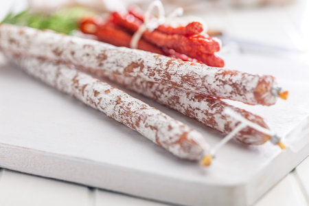 Fuet sausage with mold and smoked kabanos mini salami on a white cutting board.の写真素材