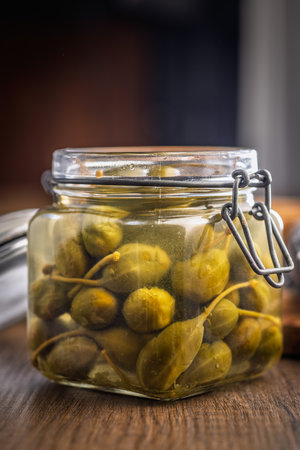 Pickled capers berries in jar on a wooden table.