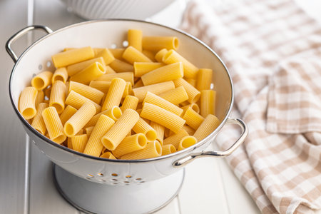 Uncooked rigatoni pasta in a colander on a white table.の写真素材