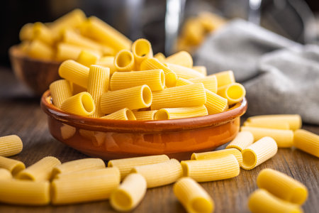 Uncooked rigatoni pasta in a bowl on a wooden table.の写真素材