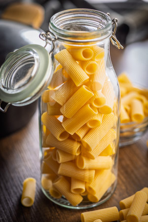 Uncooked rigatoni pasta in a jar on a wooden table.の写真素材