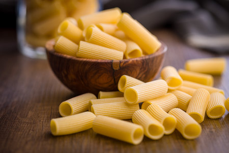 Uncooked rigatoni pasta on a wooden table.の写真素材