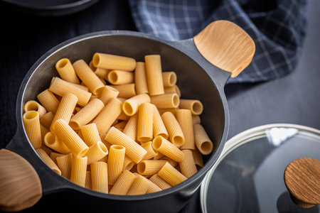 Uncooked rigatoni pasta in pot on a black table.の写真素材