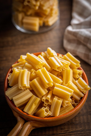 Uncooked italian pasta in a bowl on a wooden table.の写真素材