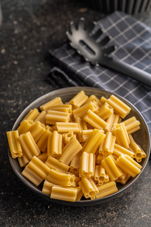 Uncooked Italian pasta in a bowl on a black table.の写真素材