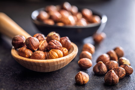 Peeled hazelnut kernels on wooden spoon on a black table.の写真素材