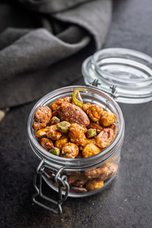 Nuts coated in sugar glaze in a jar on a black table.の写真素材