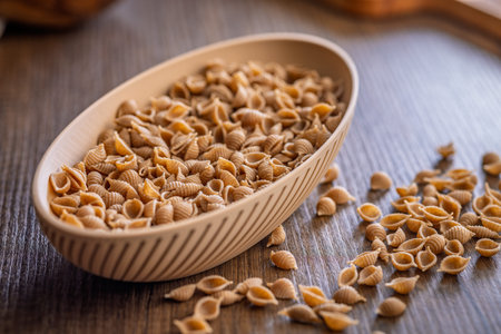 Wholegrain conchiglie pasta in bowl on a wooden table.の写真素材