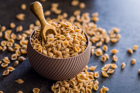 Wholegrain conchiglie pasta in bowl on a black table.の写真素材