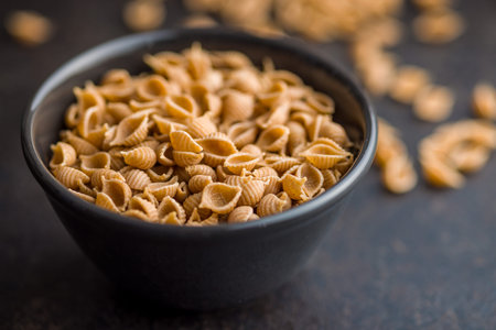 Wholegrain conchiglie pasta in bowl on a black table.の写真素材