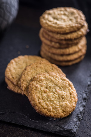 A group of oatmeal cookies is stacked neatly on a dark slate surface. Some cookies are placed next...