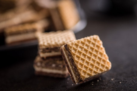 Stacked chocolate wafer biscuits with visible cream layers photographed close-up on a dark...