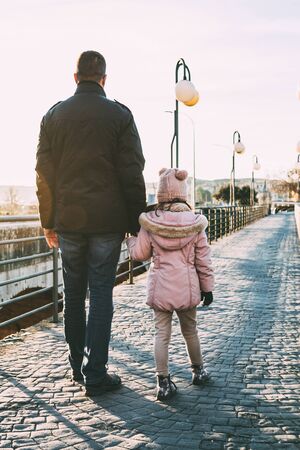 Single father walking with a little girl in a pink coat in the street on a sunny winter afternoon. Single parent family conceptの写真素材