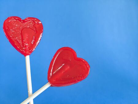 Two red heart lollipops on a blue background, tasty sweets, lovers, a gift for children. Valentine's...