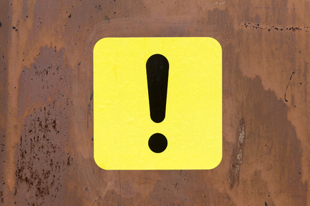 Black and yellow exclamation mark (road sign) pasted on a rusty ironの写真素材